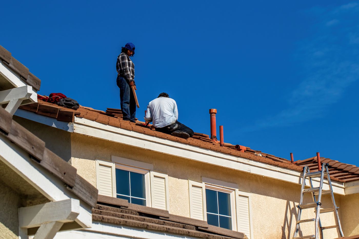 Workers repairing a tiled roof beneath a blue sky